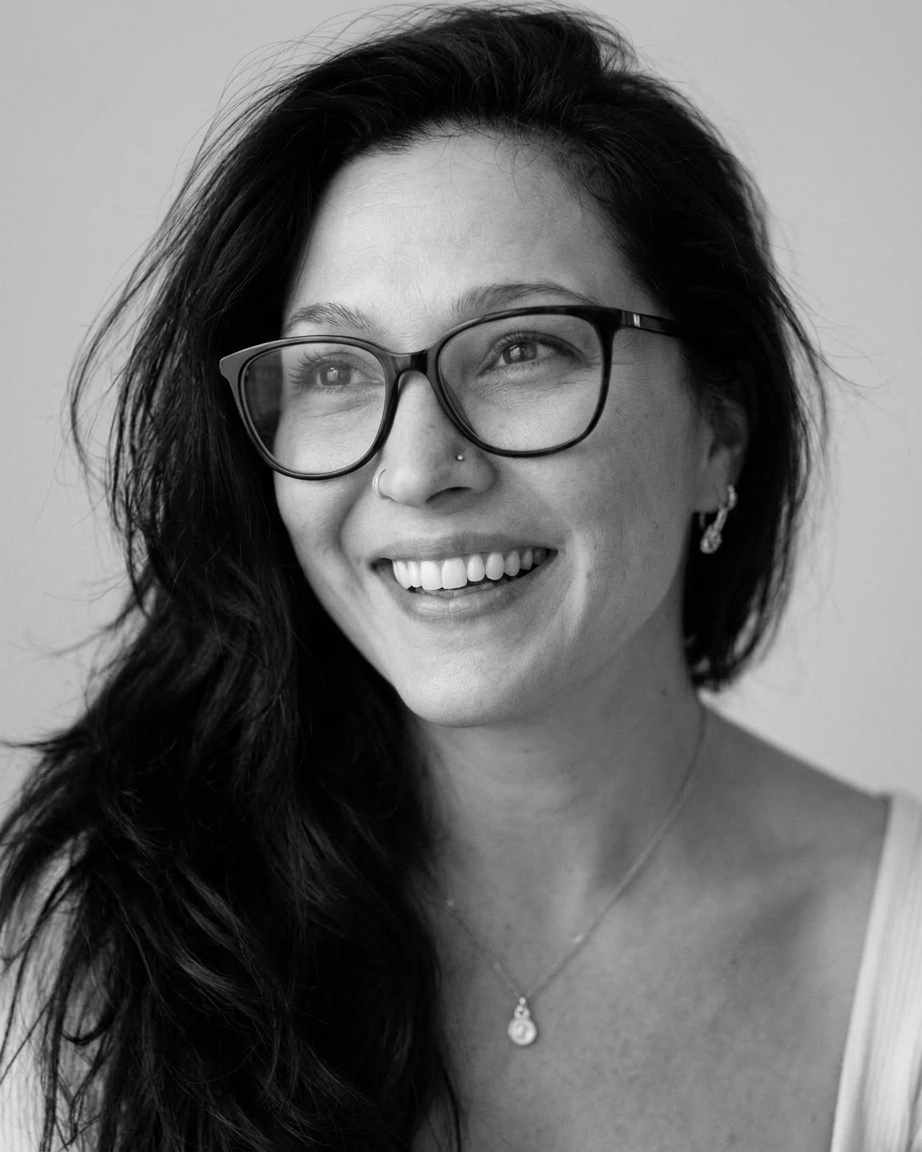 ChatGPT Image Jun 30, 2026, 11_36_53 AM Black and white portrait of a smiling woman with long dark hair, wearing glasses and a necklace.